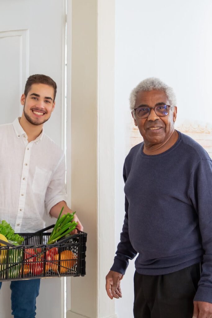 Senior man receiving fresh produce from a young volunteer indoors, promoting community support.