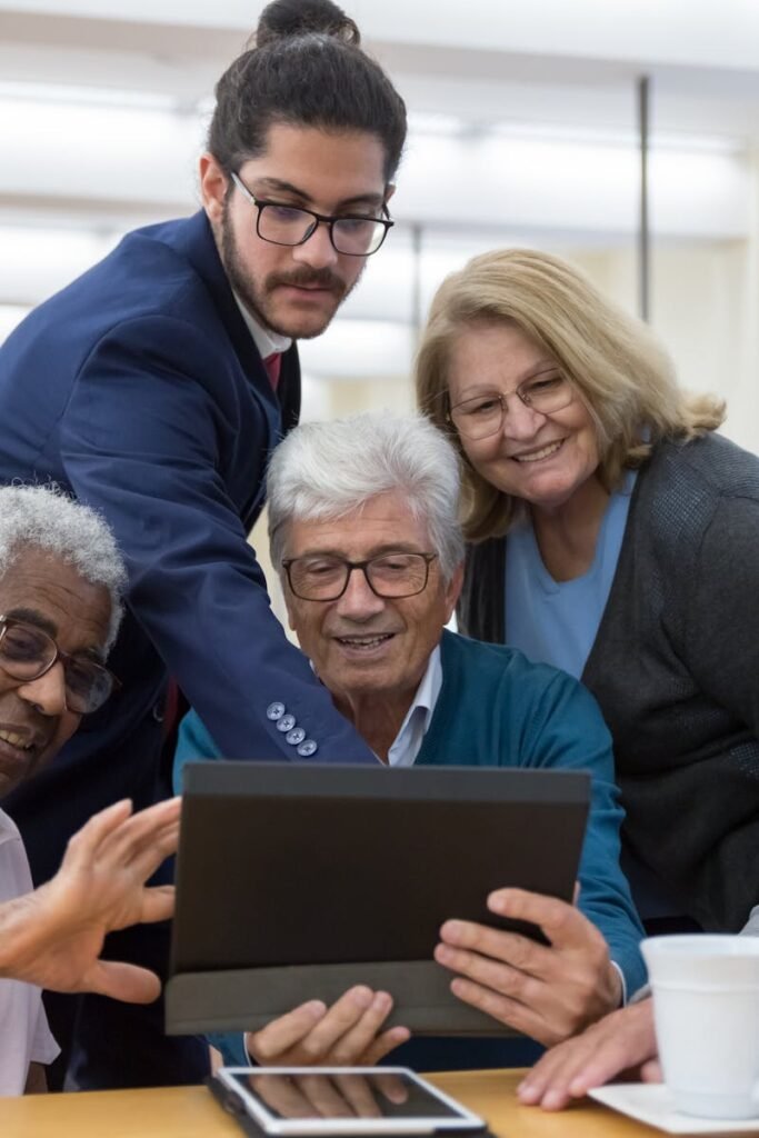Group of seniors and a young man collaborating using a tablet during a meeting indoors.